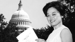 A young Patsy Mink stands in front of the capitol building holding a document.